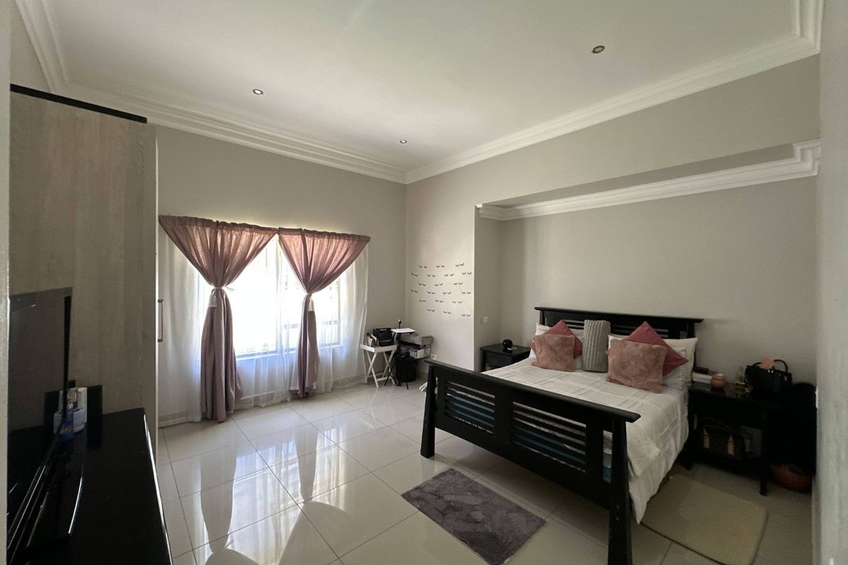 A spacious bedroom featuring neutral wall tones, polished floor tiles, recessed ceiling lighting, and decorative crown molding.
