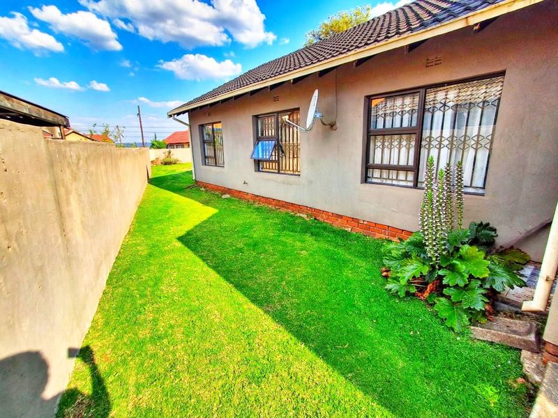 Rear exterior view of the house featuring a lawn, boundary wall, and security bars on the windows.