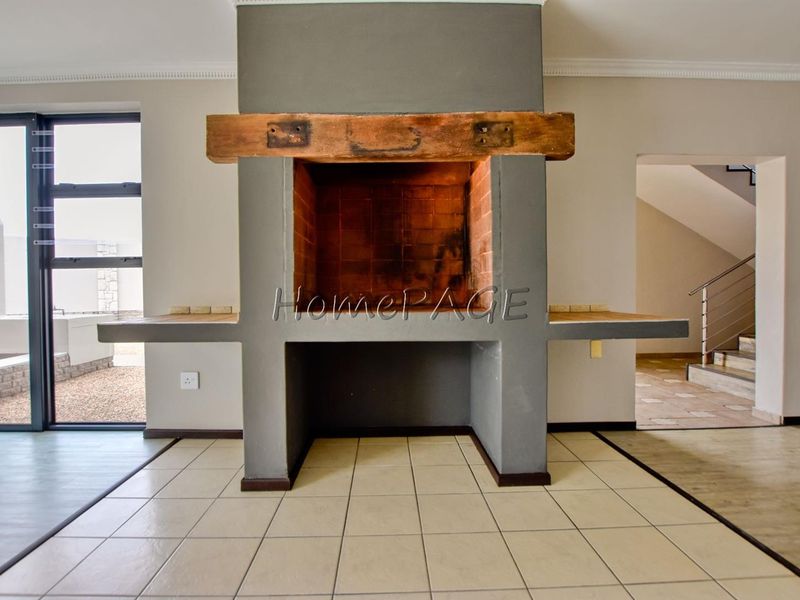 An empty living area featuring a prominent built-in fireplace with a timber mantelpiece and tiled flooring, leading to an adjacent staircase.