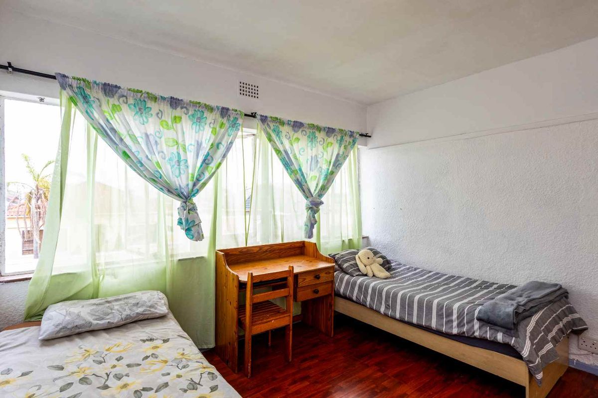 A bedroom featuring large windows, wooden flooring, and a textured wall finish, providing a functional space with natural light.
