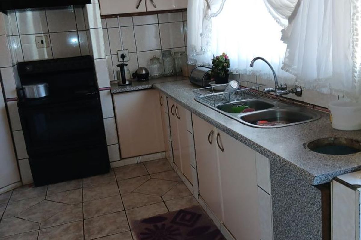 A functional kitchen featuring tiled flooring, built-in cabinetry, a double basin sink, and a freestanding stove with an extractor fan.