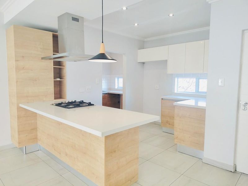 Modern kitchen featuring light wood-tone cabinetry, stone countertops, a gas hob with extractor fan, and neutral tiled flooring.