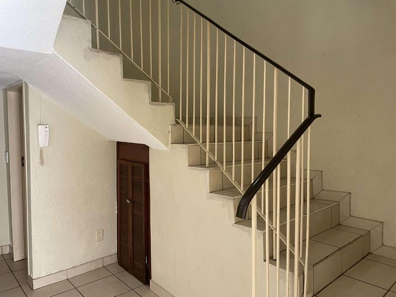A functional hallway featuring a tiled staircase with a metal balustrade and convenient under-stair storage cupboard.