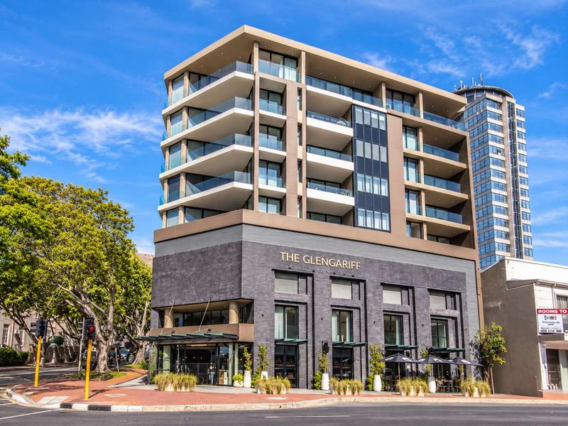 A modern multi-story apartment building featuring a dark brick ground floor, glass-fronted balconies, and contemporary architectural design on a corner street location.