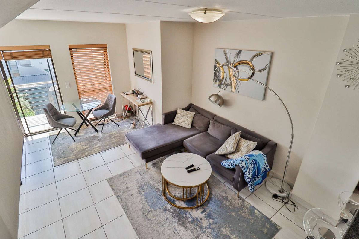 A bright, open-plan living area featuring tiled flooring, a sliding glass door leading to a balcony, and neutral wall finishes.