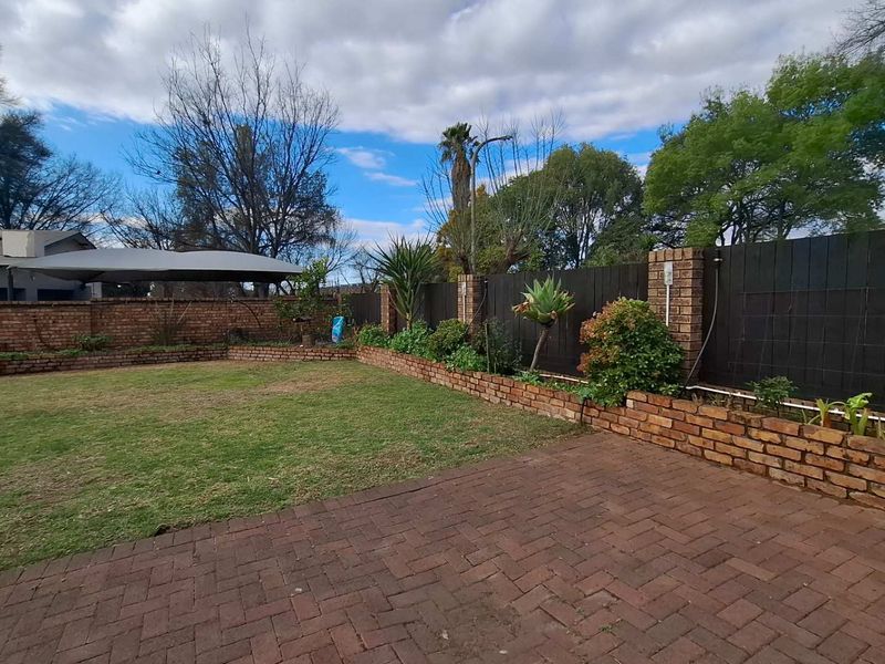 A well-maintained backyard featuring brick paving, a lawn area, and a brick retaining wall with timber fencing.