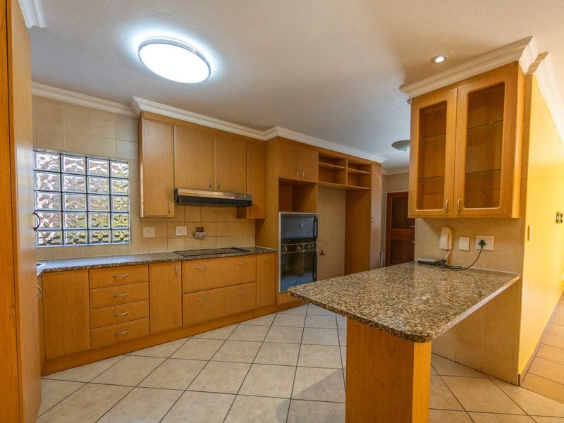 A spacious kitchen featuring wooden cabinetry, granite countertops, a breakfast bar, and a unique glass block window, offering a functional layout with classic finishes.