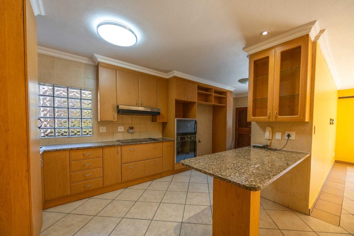 A spacious kitchen featuring wooden cabinetry, granite countertops, a breakfast bar, and a unique glass block window, offering a functional layout with classic finishes.