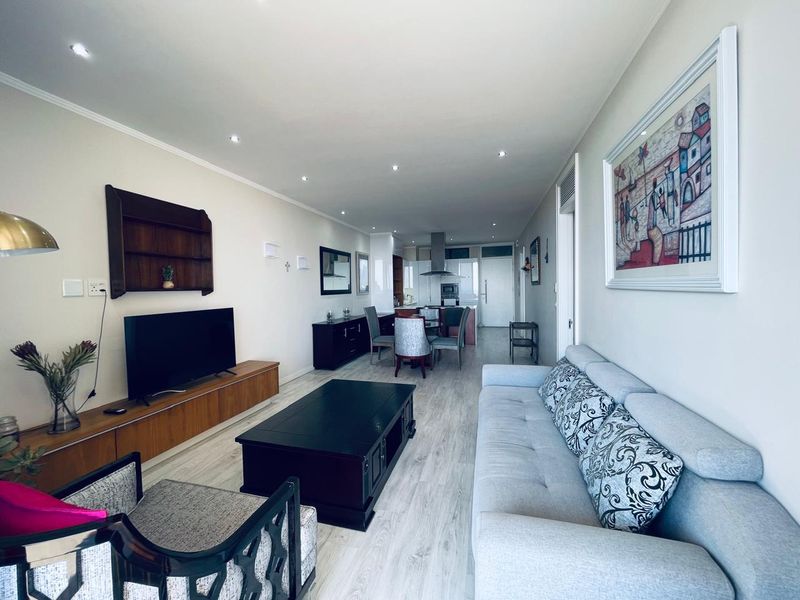 An open-plan living and dining area featuring light laminate flooring, recessed downlighting, and a modern kitchen with integrated cabinetry and extractor fan.