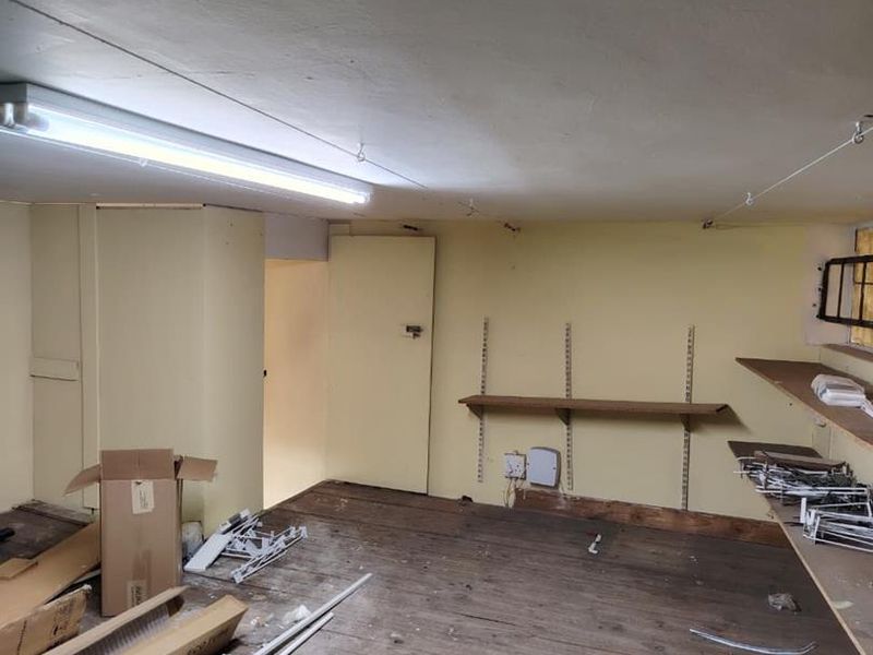 A vacant utility or storage space featuring timber flooring, wall-mounted shelving tracks, and fluorescent lighting, requiring cosmetic refurbishment.