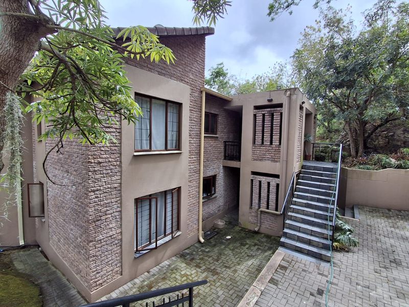 Rear exterior view of a multi-story apartment building featuring brick facade, paved courtyard, and an external staircase with metal railings.