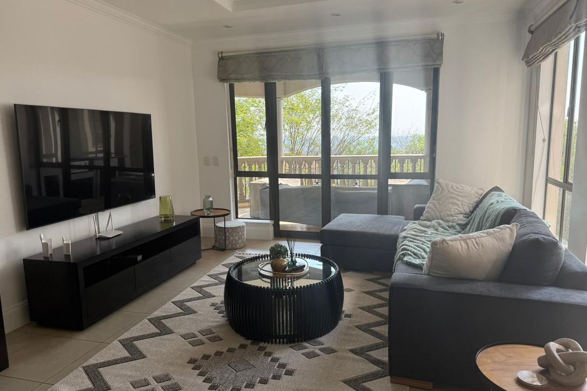 A bright and modern living room featuring tiled floors, recessed ceiling details, and large sliding glass doors that open onto a balcony with scenic views.