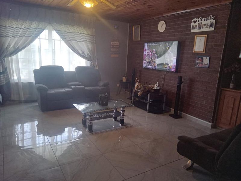 A living room featuring an exposed timber ceiling, tiled flooring, and a prominent exposed brick feature wall.