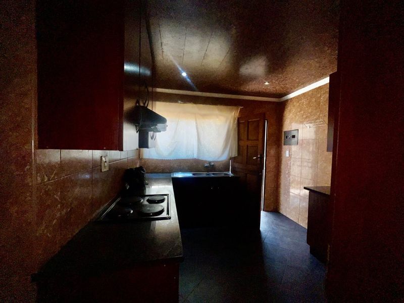 A dated kitchen featuring dark cabinetry, tiled walls, an electric hob with extractor fan, and a double sink, requiring modernization to improve functionality and aesthetics.