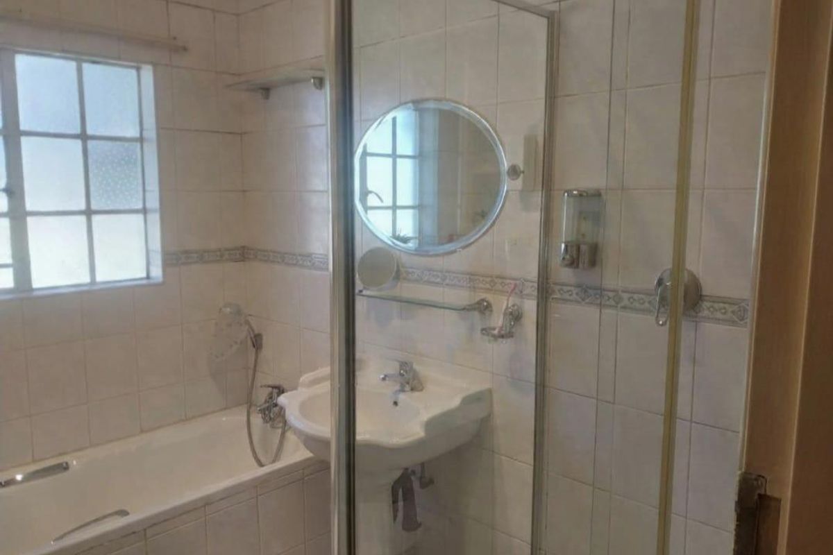 A functional bathroom featuring a built-in bathtub, a separate glass-enclosed shower, and a wall-mounted basin with tiled walls.