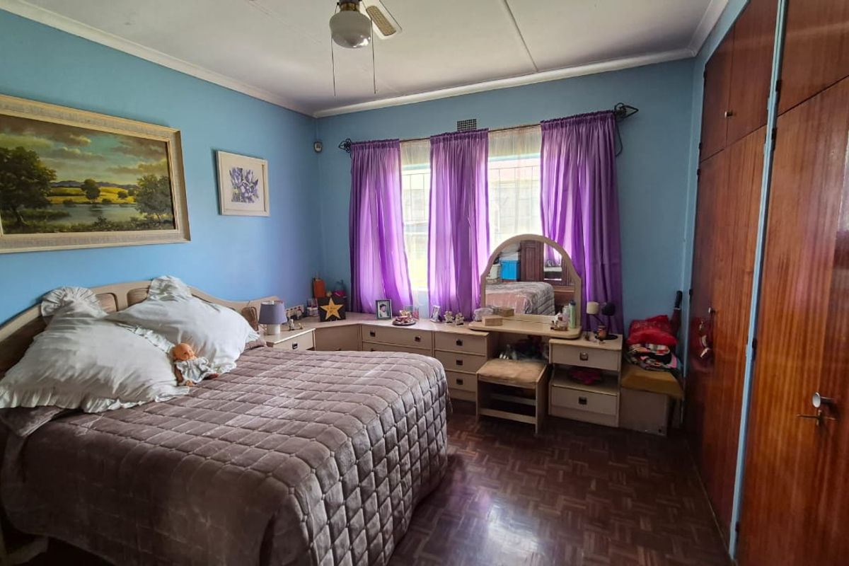 A bedroom featuring parquet flooring and extensive built-in wooden cupboards, offering a functional layout with natural light.