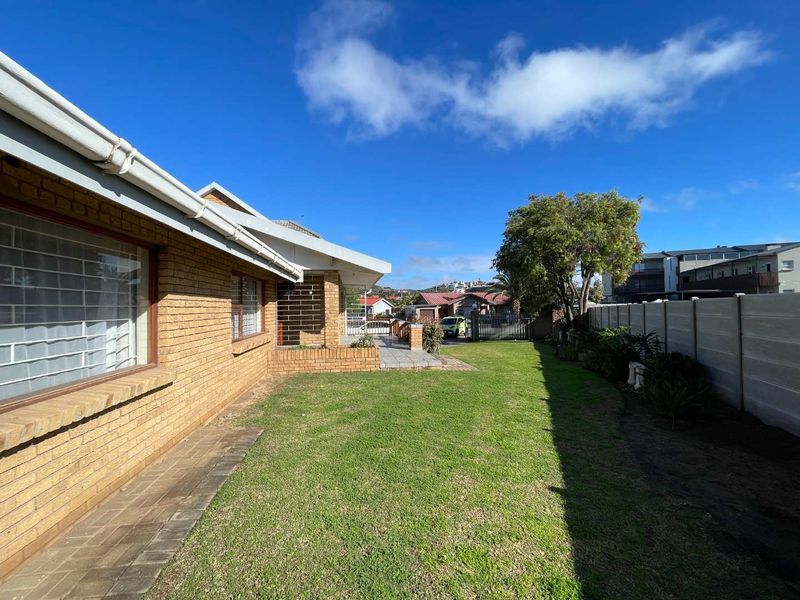 A view of the rear garden featuring a brick exterior, paved walkway, and precast concrete boundary wall.