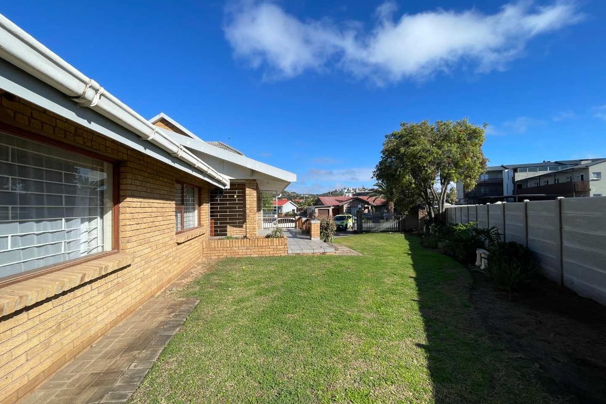 A view of the rear garden featuring a brick exterior, paved walkway, and precast concrete boundary wall.