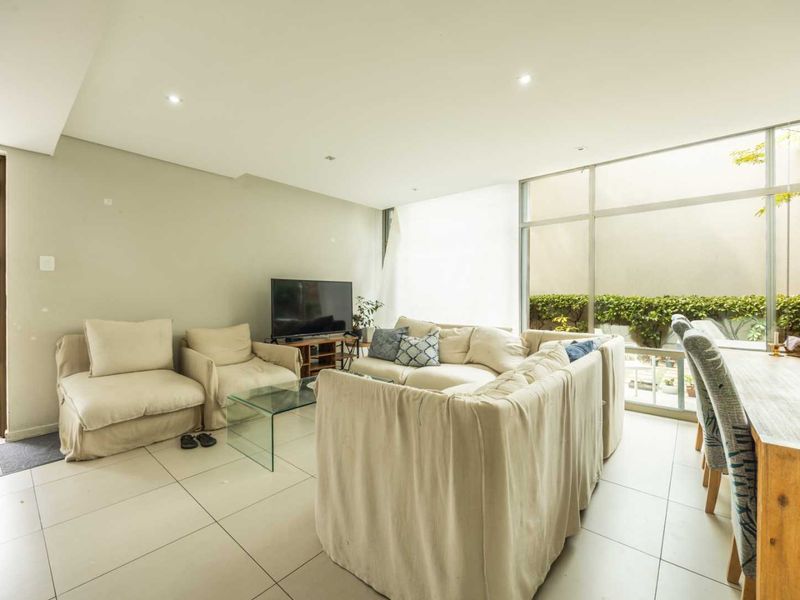 Spacious open-plan living and dining area featuring large floor-to-ceiling windows that provide ample natural light and a view of the outdoor greenery.