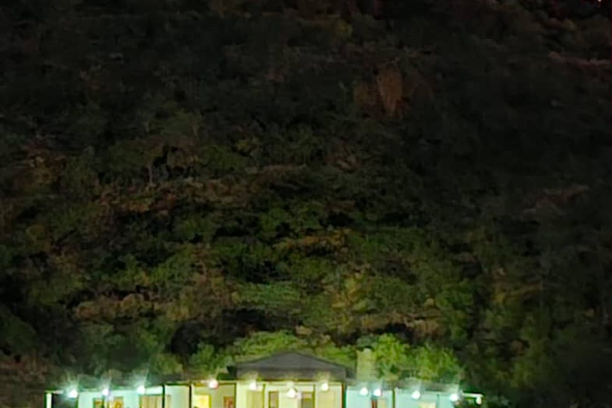 A night view of the property exterior featuring a covered patio area set against a hillside backdrop.