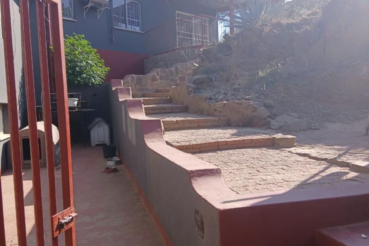 Rear exterior view featuring a stone retaining wall, brick staircase, and solar water heater mounted on the building facade.