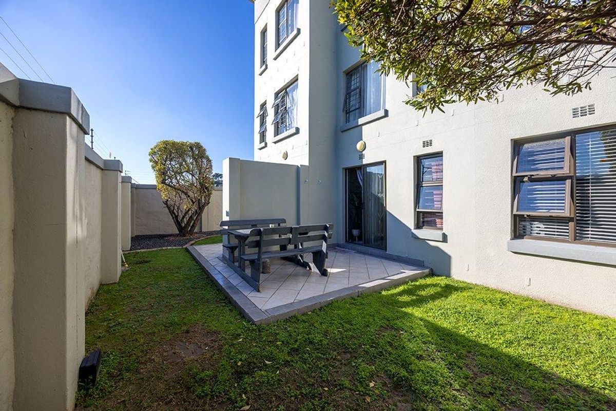 Rear exterior view of the apartment featuring a private tiled patio area, small garden space, and secure boundary walling.