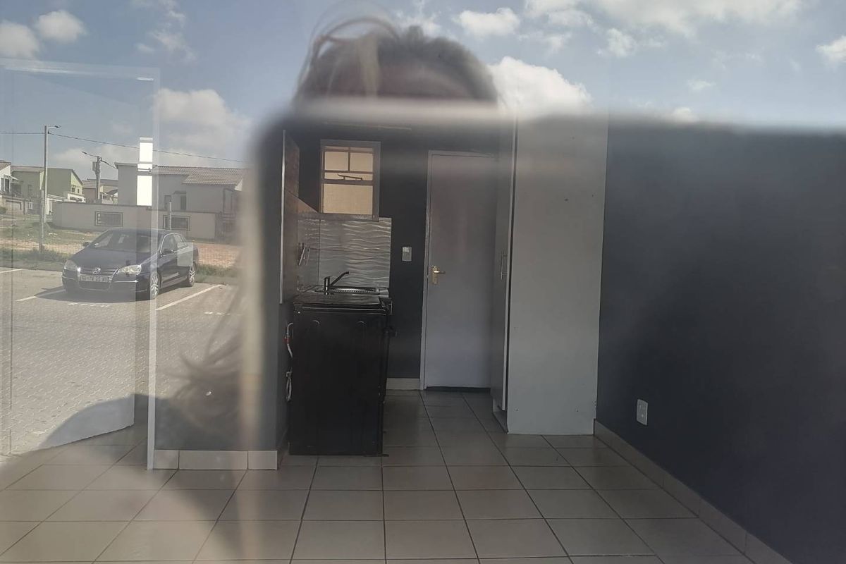 A view through a window into a small, empty kitchen area featuring tiled floors, a sink, and built-in cabinetry.