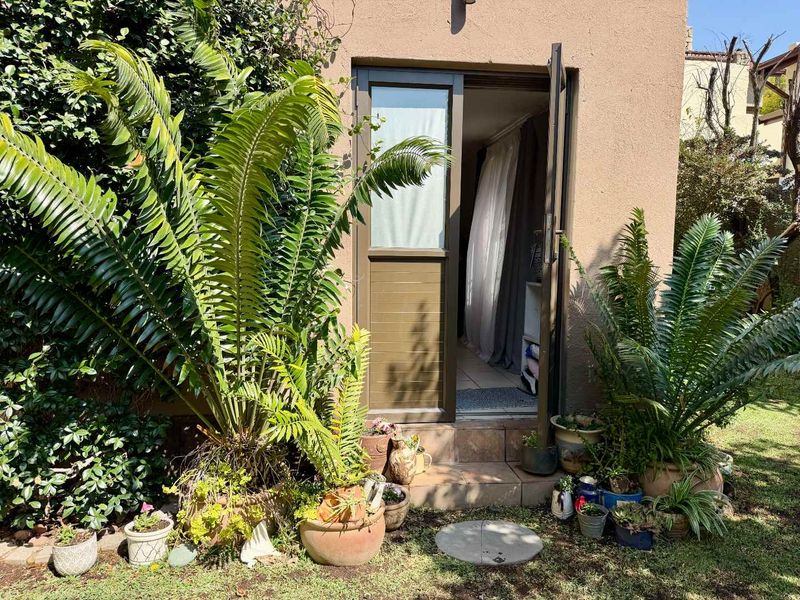 A rear exterior view of a cottage featuring a tiled step leading to an aluminium door, surrounded by established garden greenery.