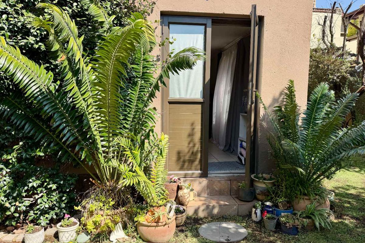 A rear exterior view of a cottage featuring a tiled step leading to an aluminium door, surrounded by established garden greenery.