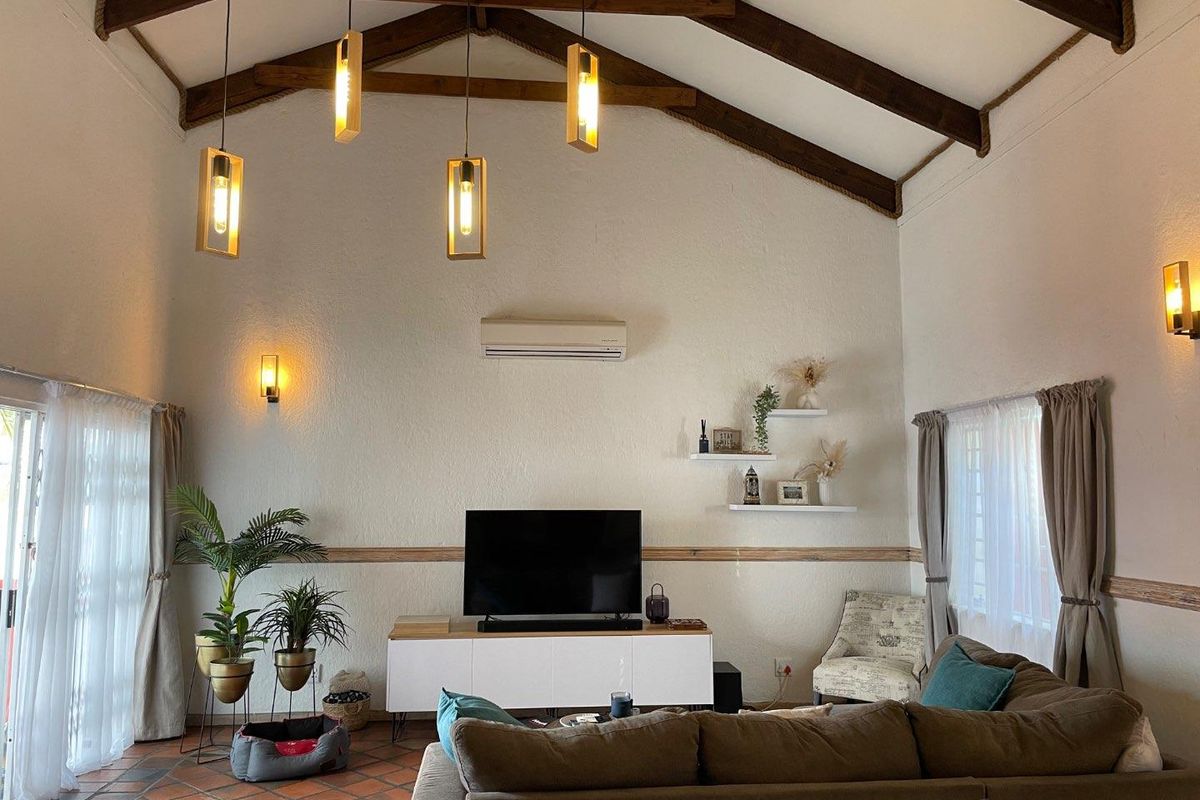 Spacious living area featuring high vaulted ceilings with exposed timber beams, terracotta tile flooring, and wall-mounted air conditioning unit.