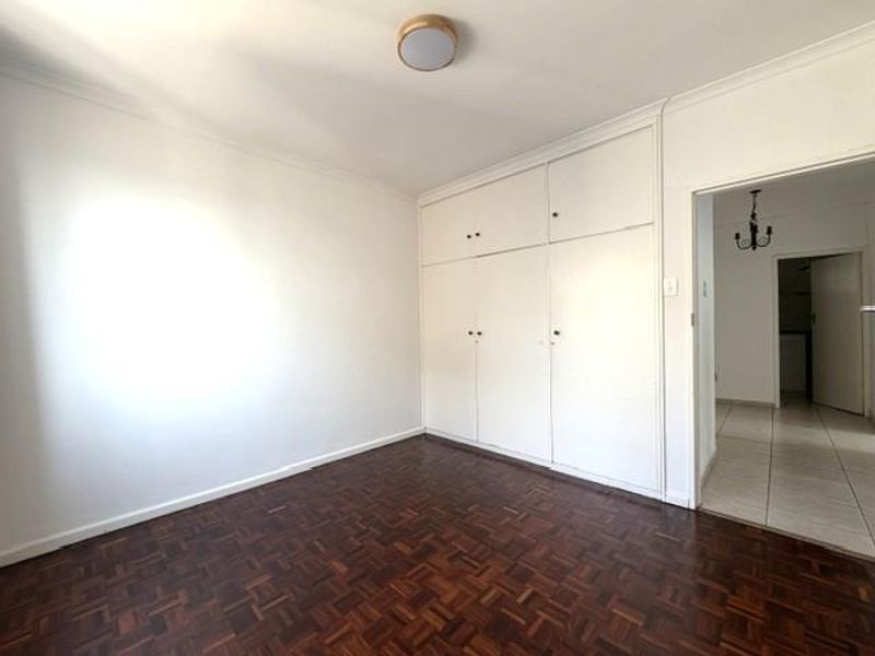 A bright, empty bedroom featuring classic parquet flooring and ample built-in cupboard storage space.
