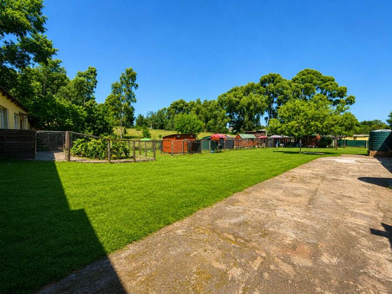 A spacious, well-maintained garden area featuring a large lawn, perimeter fencing, and a water tank, with a paved walkway along the side.