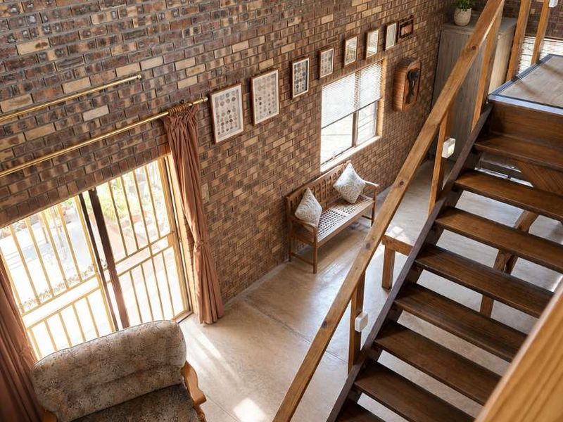 A double-volume living area featuring a prominent exposed brick wall, wooden staircase, and large sliding doors providing access to the exterior.