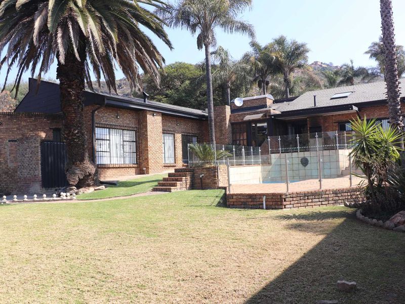 Rear view of the property featuring a brick facade, a swimming pool with glass fencing, a paved patio area, and a landscaped garden.