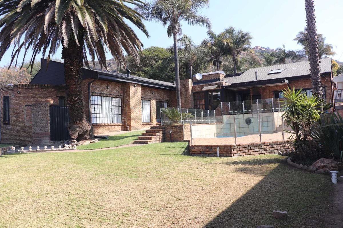 Rear view of the property featuring a brick facade, a swimming pool with glass fencing, a paved patio area, and a landscaped garden.