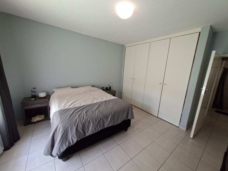 A functional bedroom featuring neutral wall tones, tiled flooring, and ample built-in cupboard storage space.