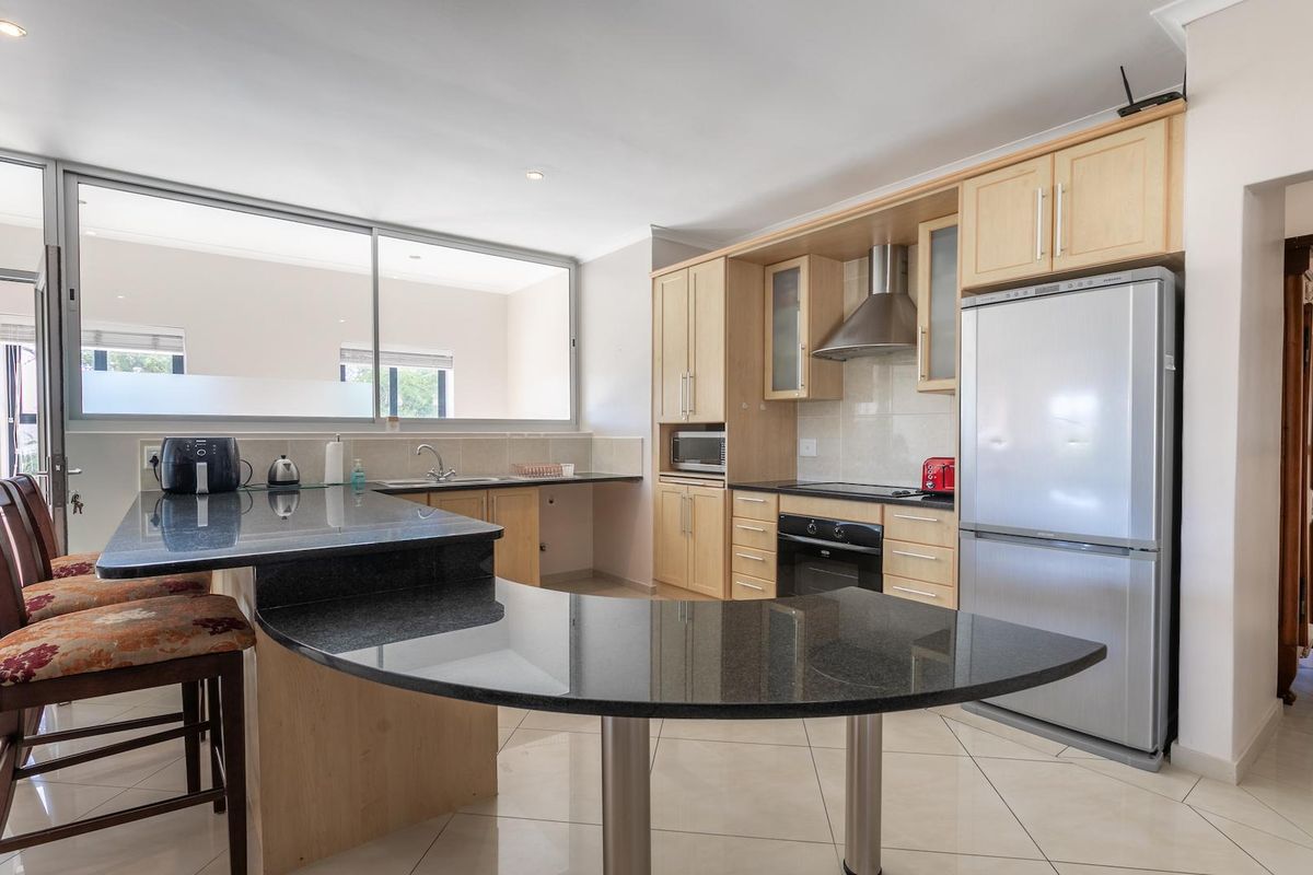 Modern kitchen featuring light wood cabinetry, granite countertops, a breakfast bar, built-in oven, extractor fan, and tiled flooring.