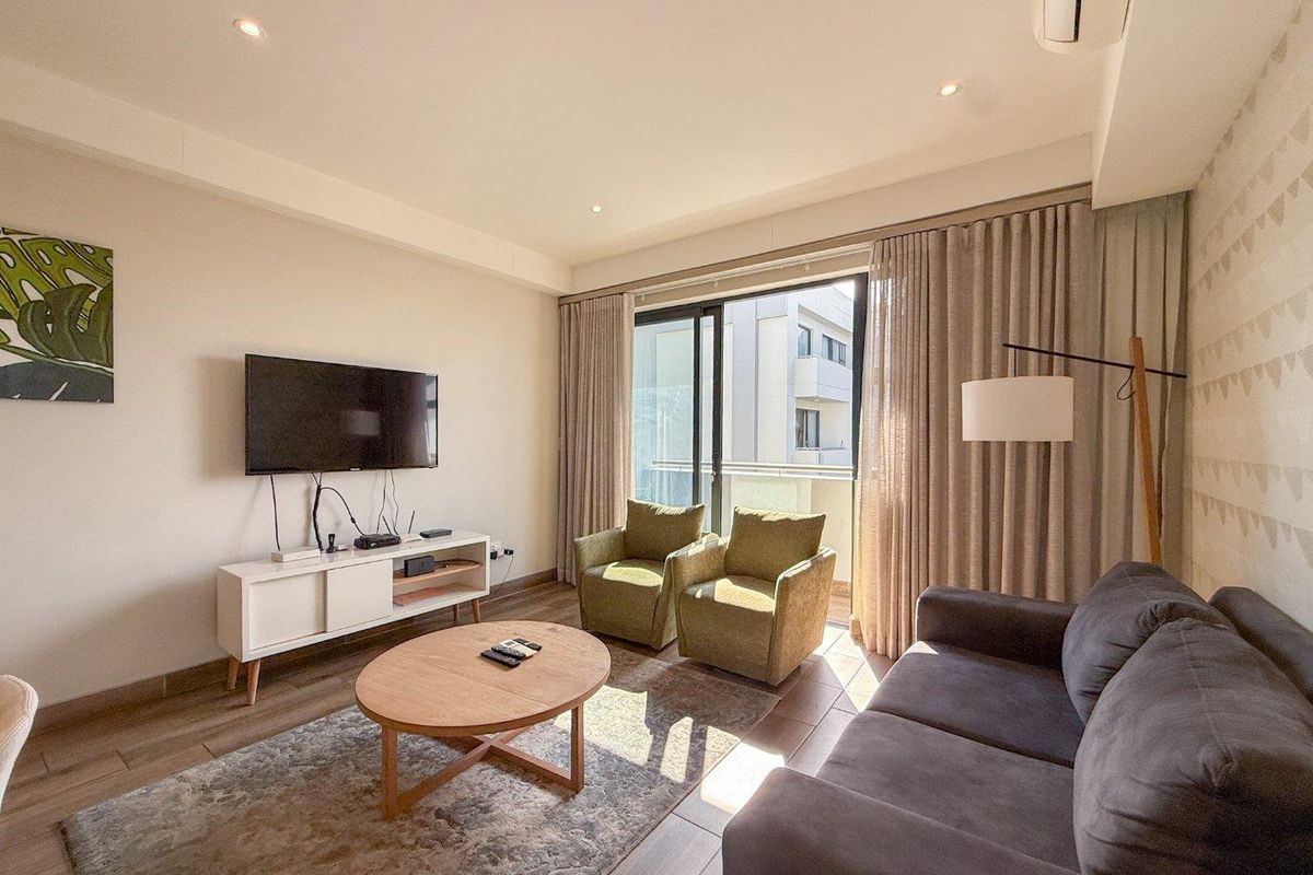 A bright and modern living room featuring tiled flooring, recessed ceiling lighting, a wall-mounted air conditioning unit, and large sliding glass doors to a balcony.