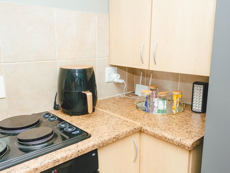 A compact kitchen area featuring laminate countertops, built-in light wood cabinetry, and a built-in electric hob with a tiled backsplash.