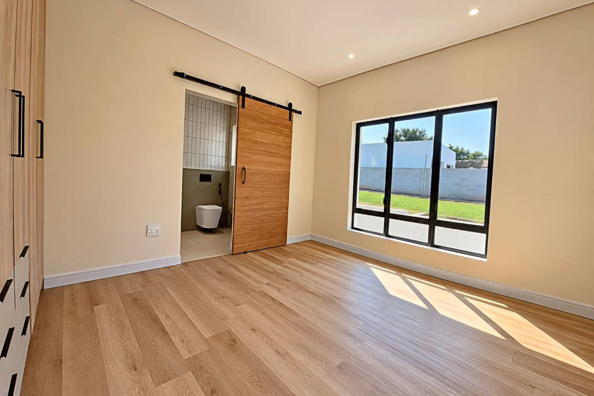 A bright, modern bedroom featuring light laminate flooring, built-in cupboards, and a stylish sliding barn door leading to an en-suite bathroom.