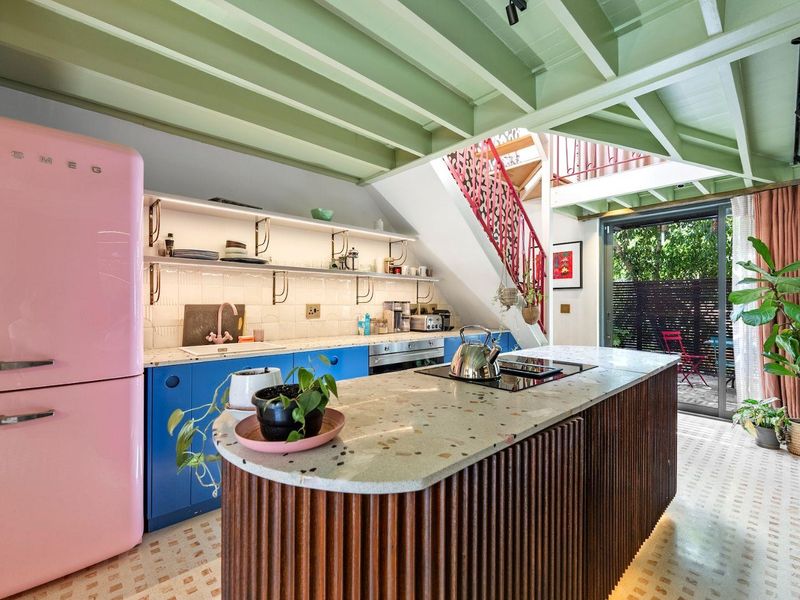 Modern kitchen featuring a central island with terrazzo countertop, open shelving, built-in appliances, and exposed timber ceiling beams, with direct access to the patio.