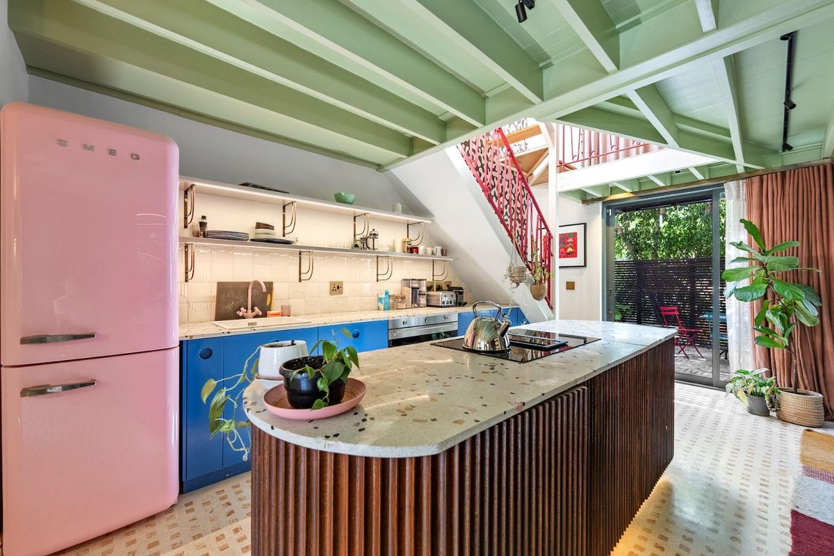 Modern kitchen featuring a central island with terrazzo countertop, open shelving, built-in appliances, and exposed timber ceiling beams, with direct access to the patio.