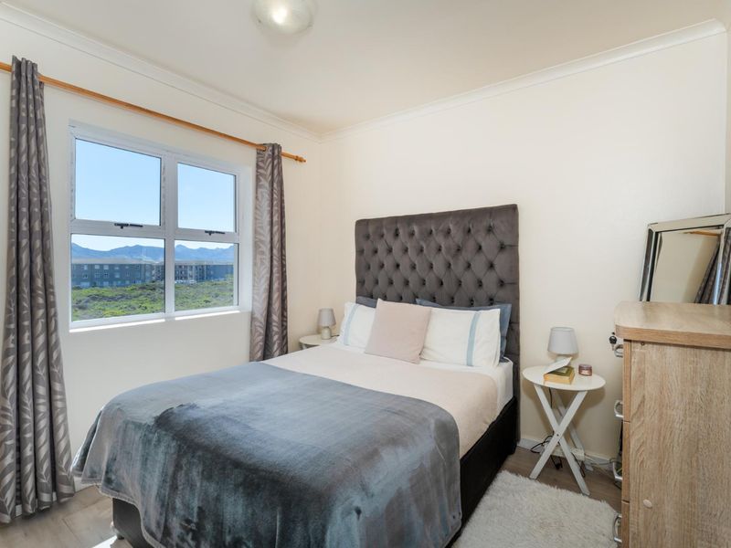A well-maintained bedroom featuring laminate flooring, coving, and an aluminium window frame with views of the surrounding area.