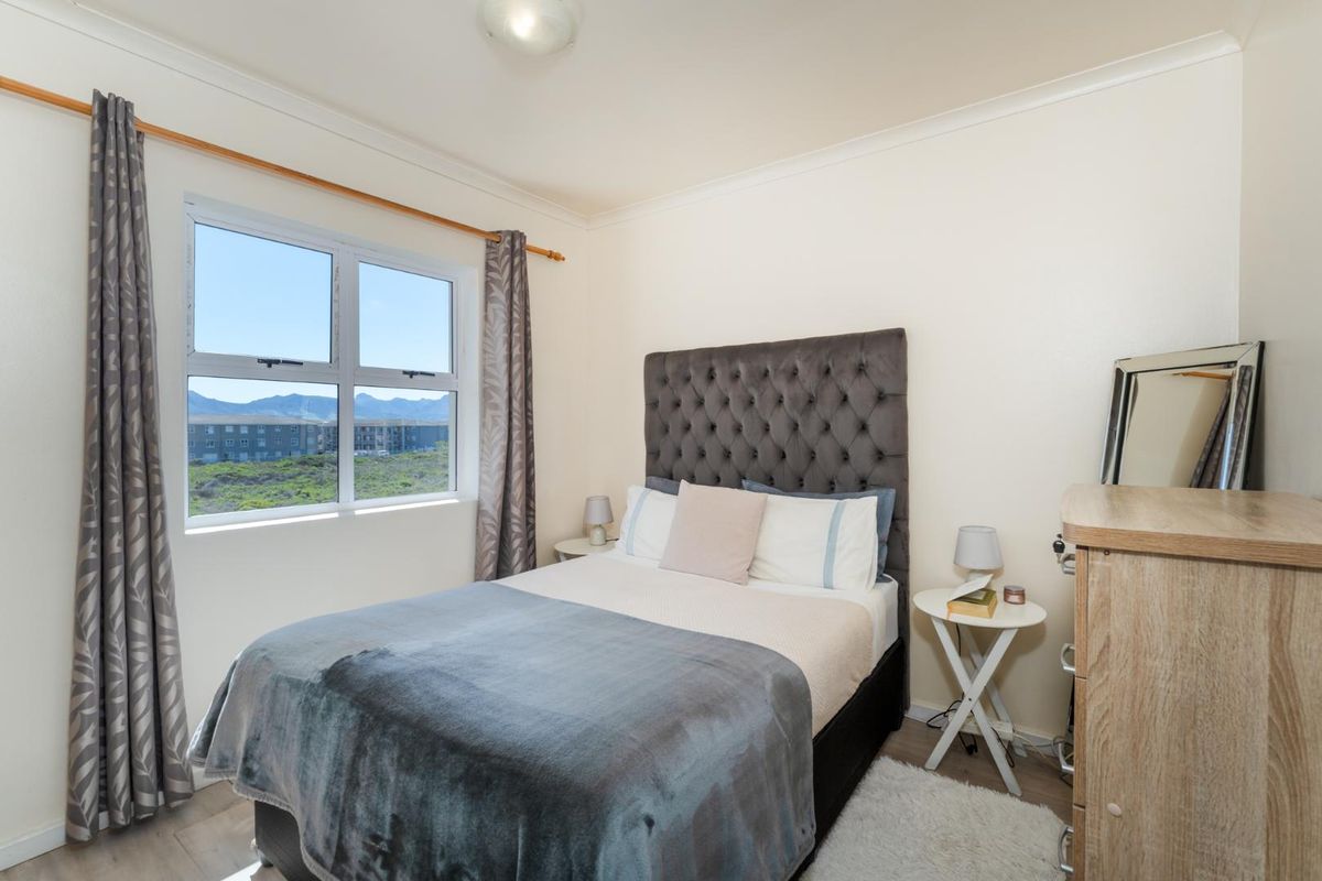 A well-maintained bedroom featuring laminate flooring, coving, and an aluminium window frame with views of the surrounding area.