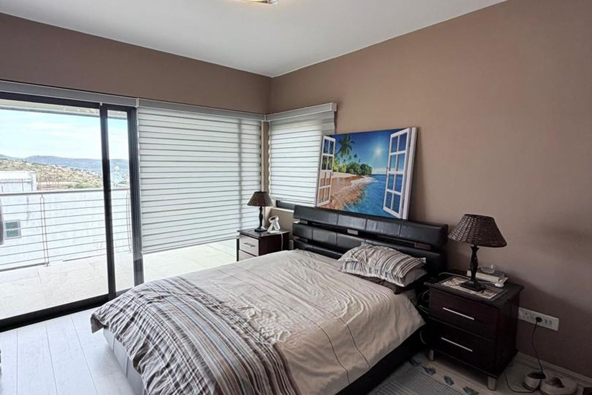 A well-lit bedroom featuring light-toned wood-look flooring, modern ceiling lighting, and large sliding glass doors that open onto a private balcony with scenic views.