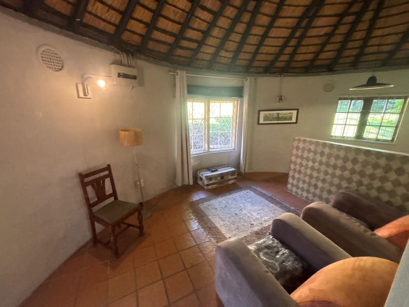 A circular living room featuring a traditional thatched roof, terracotta tiled flooring, and leaded glass windows, offering a rustic cottage aesthetic.