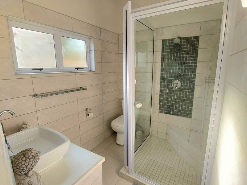 Modern bathroom featuring a glass-enclosed shower with mosaic tile accent, a vessel sink vanity, and neutral wall tiling.
