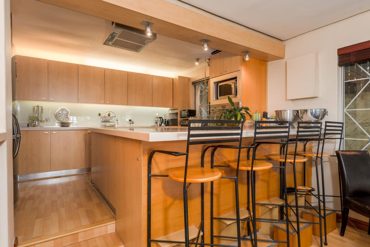 A functional kitchen featuring light wood cabinetry, a central island with breakfast bar seating, and integrated appliances.