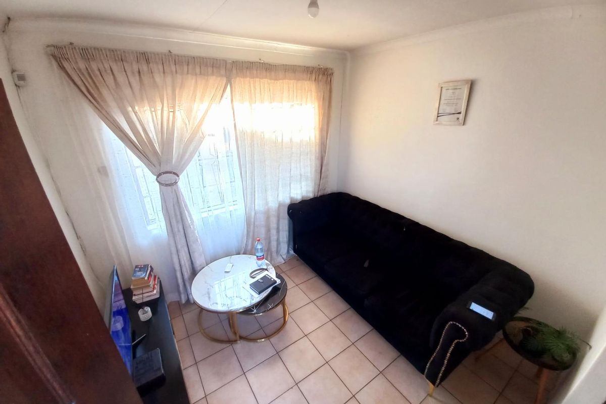 A compact living room featuring tiled flooring, a large window with curtain treatments, and standard ceiling lighting.