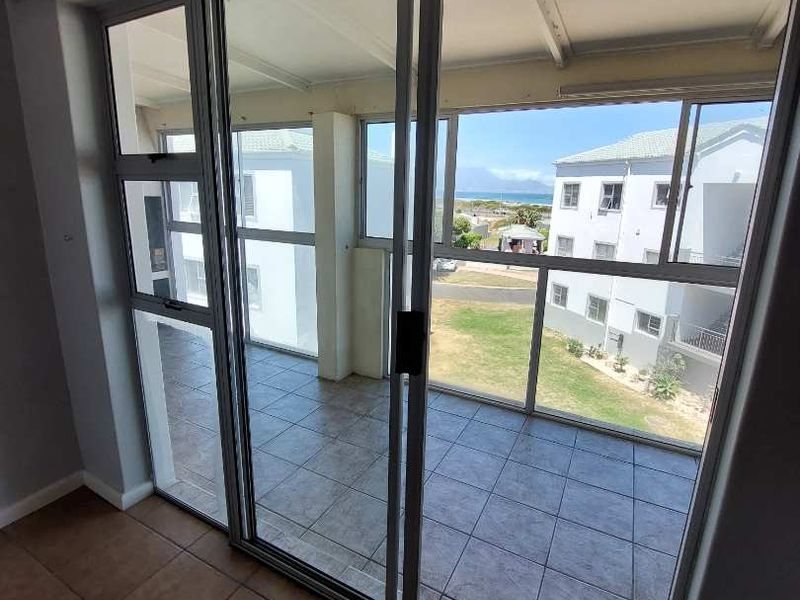 A covered balcony featuring tiled flooring and sliding glass doors, offering an outdoor space with views of the surrounding complex and distant landscape.